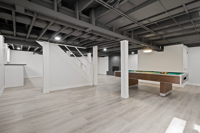 basement featuring a fireplace, light hardwood / wood-style flooring, and pool table