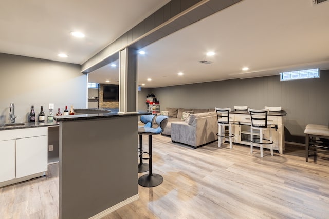 bar featuring light wood-type flooring, white cabinetry, and sink