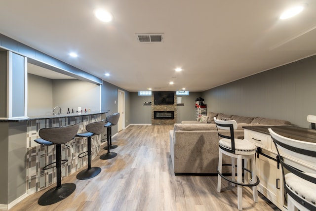 living room featuring indoor bar, light hardwood / wood-style flooring, and a stone fireplace