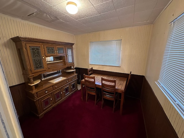 dining room featuring wood walls and dark carpet