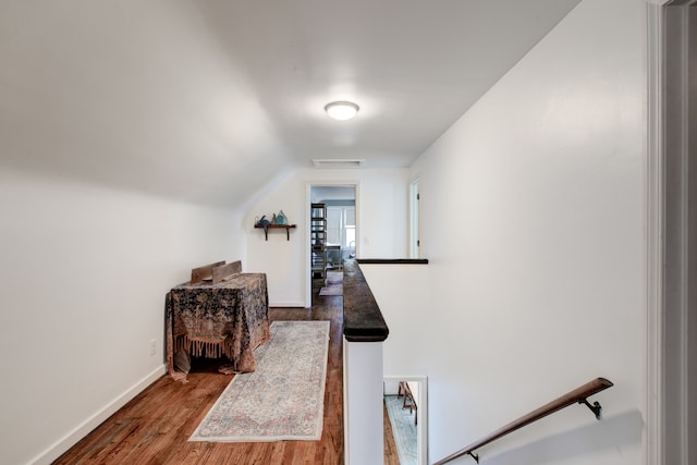 corridor with hardwood / wood-style floors and vaulted ceiling