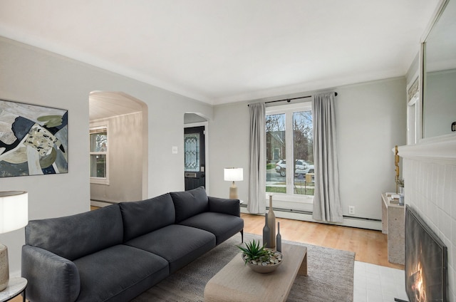 living room featuring light hardwood / wood-style floors, baseboard heating, crown molding, and a tiled fireplace