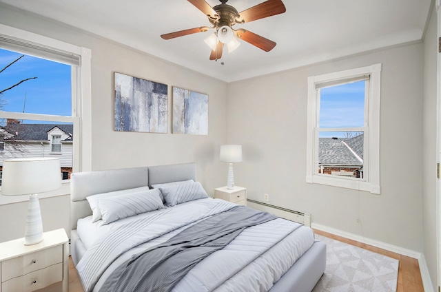 bedroom with multiple windows, ceiling fan, a baseboard heating unit, and light wood-type flooring