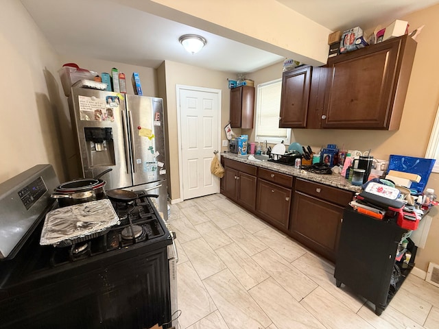 kitchen featuring sink, stainless steel fridge, light stone countertops, black gas range oven, and dark brown cabinets