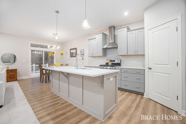 kitchen featuring gray cabinetry, sink, hanging light fixtures, wall chimney range hood, and stainless steel range with gas stovetop