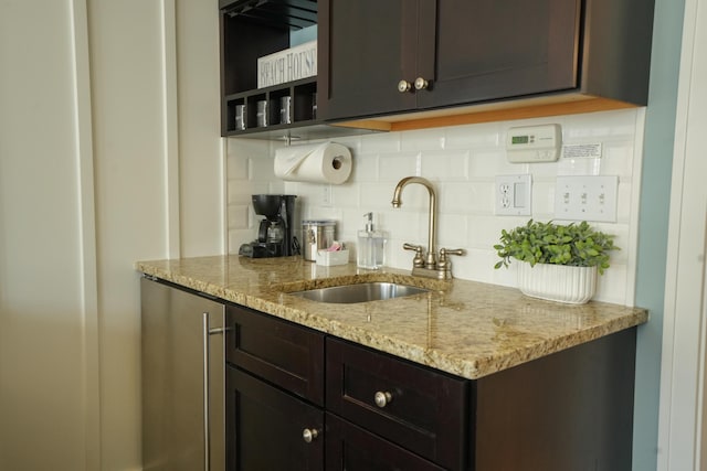 kitchen featuring tasteful backsplash, dark brown cabinetry, light stone countertops, and sink