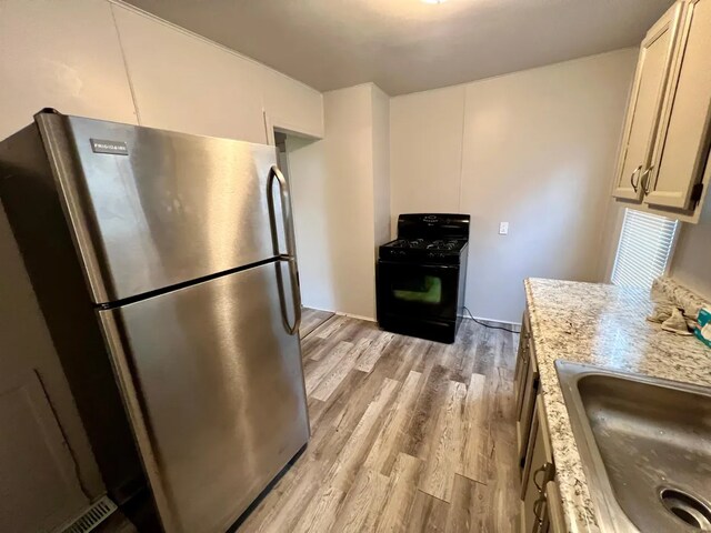 kitchen featuring light stone countertops, light wood-type flooring, sink, black gas range, and stainless steel refrigerator