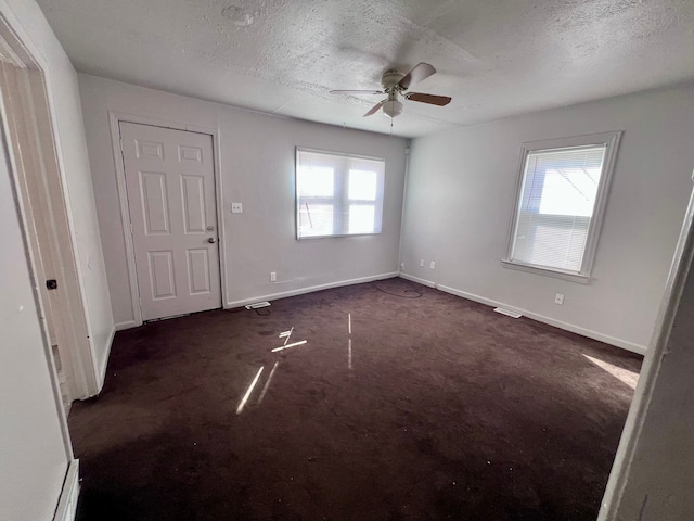 unfurnished room featuring baseboards, a textured ceiling, and dark carpet