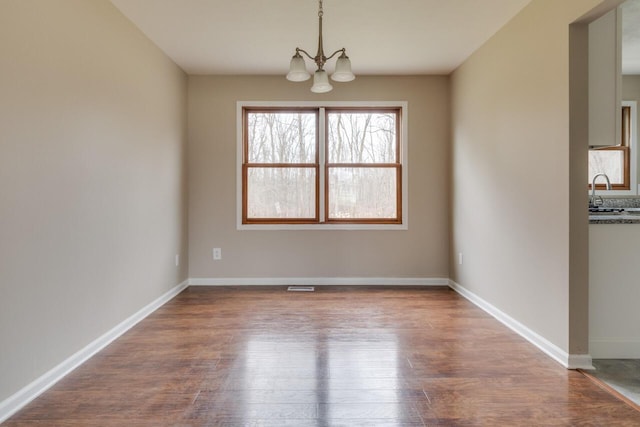 unfurnished dining area with wood-type flooring, an inviting chandelier, and sink