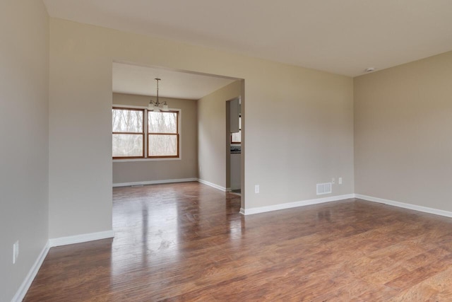 empty room with a chandelier and dark wood-type flooring