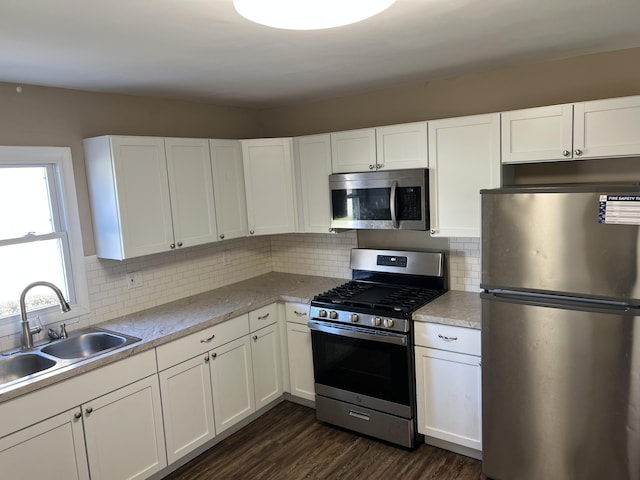 kitchen featuring appliances with stainless steel finishes, backsplash, dark wood-type flooring, sink, and white cabinetry