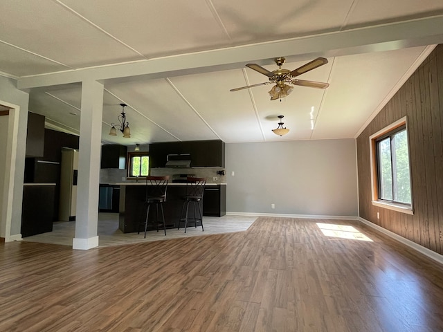 unfurnished living room featuring wood walls, lofted ceiling with beams, ceiling fan with notable chandelier, and hardwood / wood-style flooring