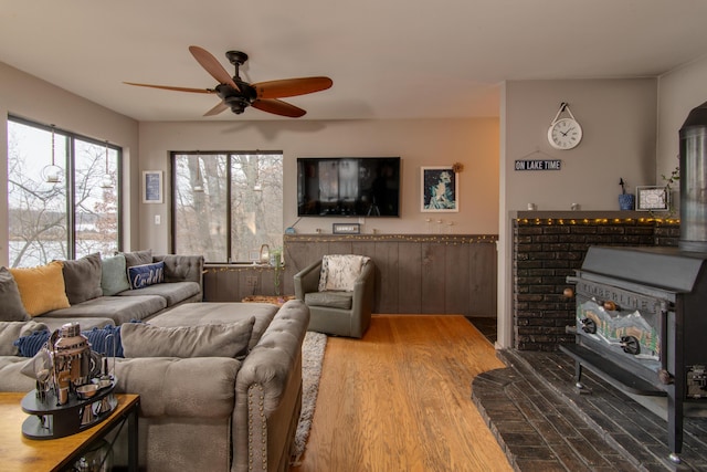 living area featuring ceiling fan, wood finished floors, and a wood stove