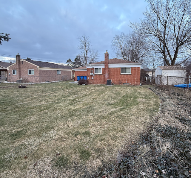 back of property featuring brick siding, a chimney, fence, and a lawn