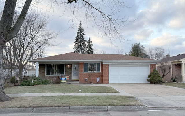 single story home featuring a garage, concrete driveway, roof with shingles, a front lawn, and brick siding