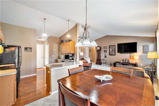 dining area featuring sink, a chandelier, vaulted ceiling, and light hardwood / wood-style floors