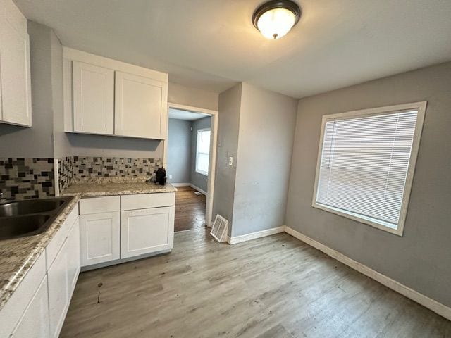 kitchen with white cabinets, tasteful backsplash, light stone counters, and light hardwood / wood-style floors