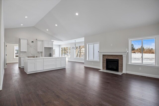 unfurnished living room featuring high vaulted ceiling, dark wood-style flooring, a fireplace with flush hearth, and baseboards