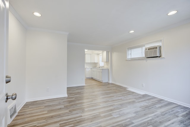 unfurnished living room with crown molding, a wall unit AC, sink, and light hardwood / wood-style flooring