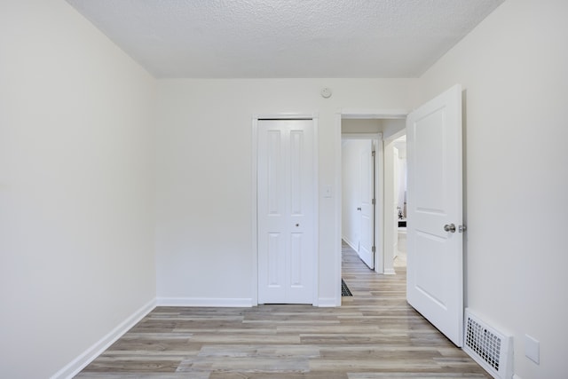 unfurnished bedroom featuring light hardwood / wood-style floors, a textured ceiling, and a closet