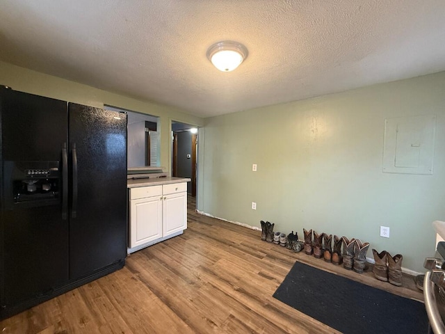 kitchen with white cabinetry, black fridge, electric panel, a textured ceiling, and light wood-type flooring