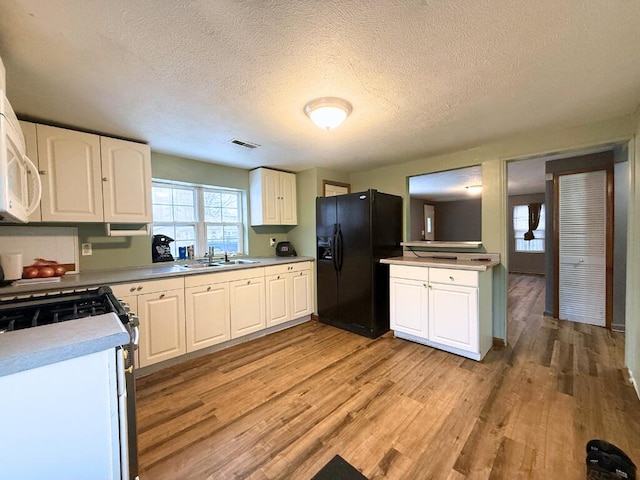 kitchen featuring white cabinetry, black fridge, sink, and stove