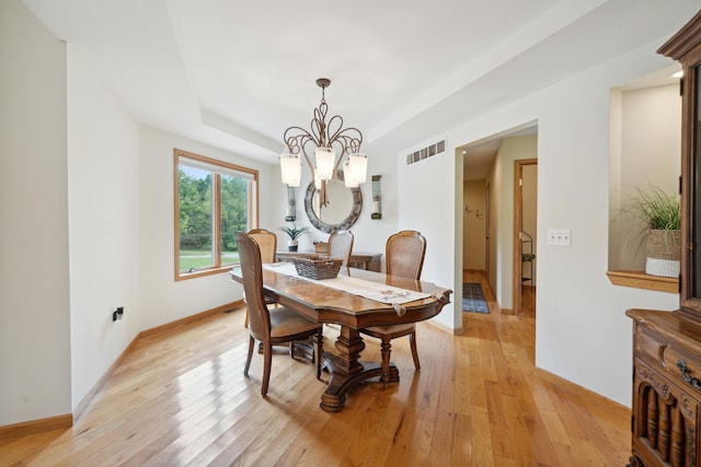 dining room with light wood-type flooring, a chandelier, and a tray ceiling