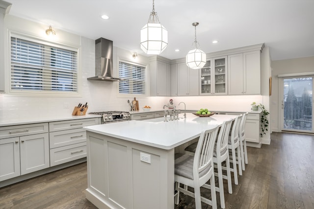 kitchen featuring dark hardwood / wood-style flooring, wall chimney exhaust hood, an island with sink, and stainless steel range oven