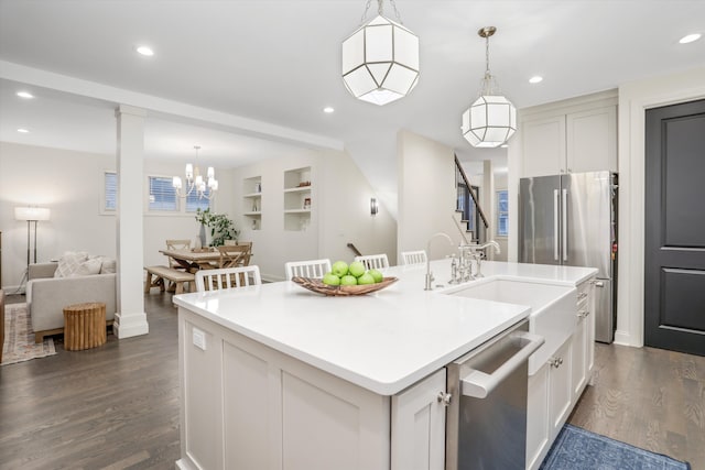 kitchen featuring built in shelves, stainless steel appliances, a kitchen island with sink, sink, and hanging light fixtures