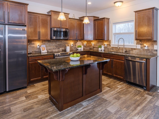 kitchen with appliances with stainless steel finishes, sink, decorative light fixtures, dark stone countertops, and a kitchen island