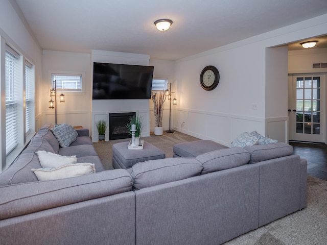 carpeted living area featuring a fireplace, visible vents, a decorative wall, and wainscoting