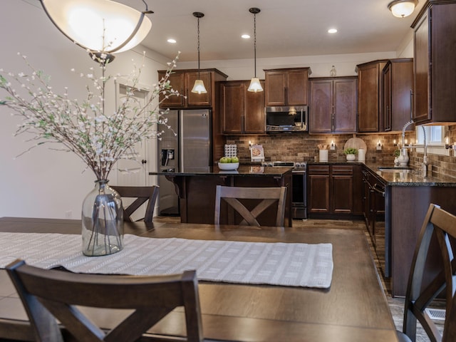 kitchen with appliances with stainless steel finishes, backsplash, dark stone countertops, pendant lighting, and a sink