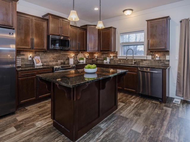 kitchen with pendant lighting, stainless steel appliances, dark brown cabinetry, a sink, and dark stone countertops