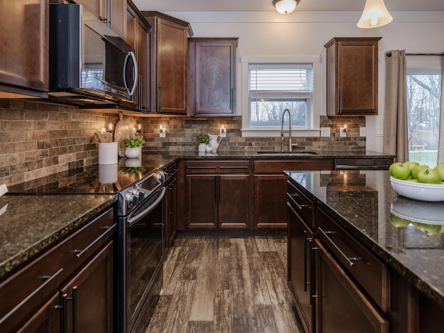 kitchen with dark brown cabinets, dark stone counters, stainless steel appliances, and a sink