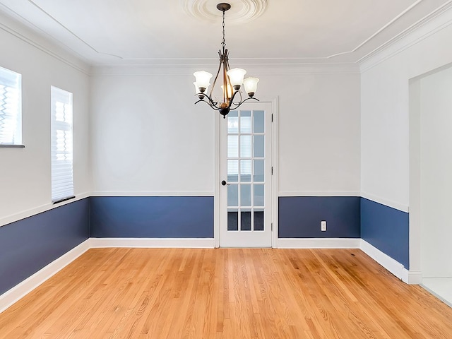 empty room featuring wood-type flooring, ornamental molding, and an inviting chandelier