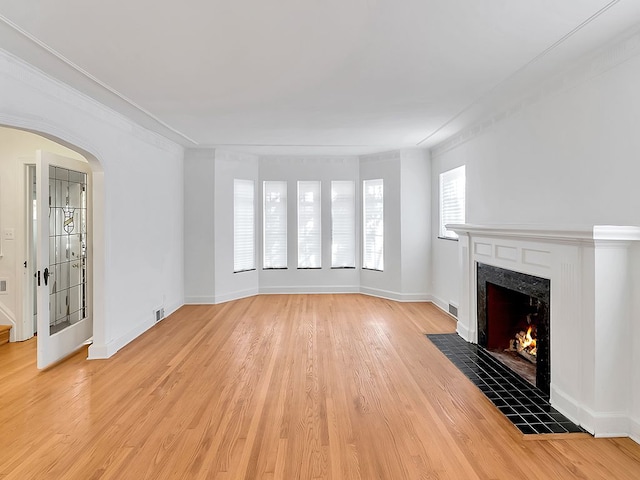 unfurnished living room with light wood-type flooring, ornamental molding, and a tile fireplace