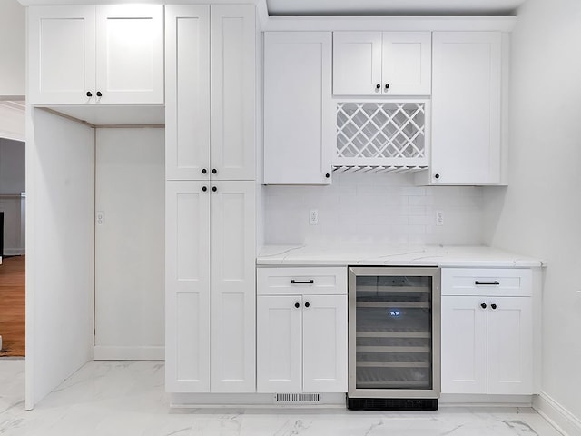 bar with decorative backsplash, light stone countertops, white cabinets, and beverage cooler