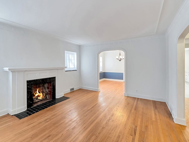 unfurnished living room featuring a tile fireplace, a chandelier, ornamental molding, and light hardwood / wood-style floors