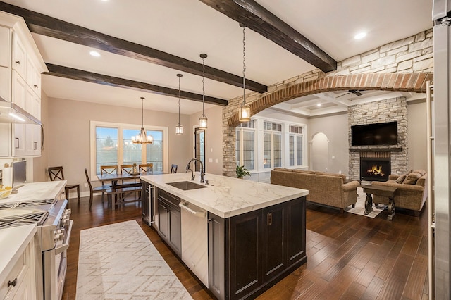 kitchen with beam ceiling, pendant lighting, a kitchen island with sink, a fireplace, and appliances with stainless steel finishes