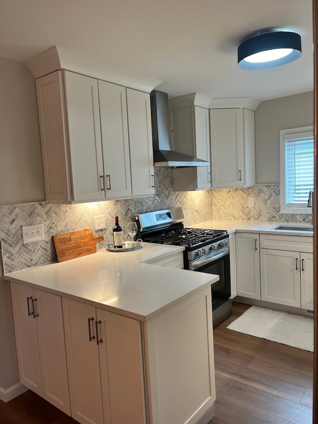 kitchen featuring stainless steel gas range oven, sink, white cabinets, and wall chimney exhaust hood