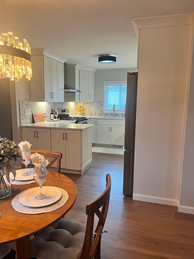 kitchen featuring wall chimney range hood, white cabinetry, stainless steel appliances, decorative backsplash, and decorative light fixtures