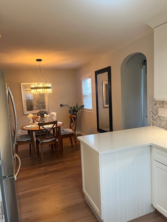 kitchen with stainless steel refrigerator, tasteful backsplash, wood-type flooring, white cabinets, and hanging light fixtures