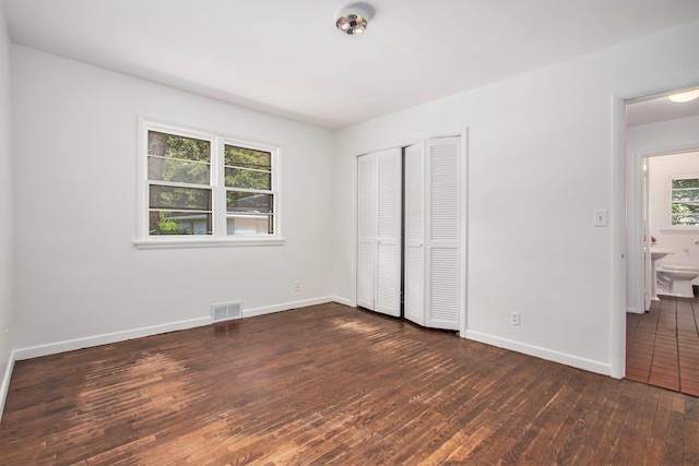 unfurnished bedroom with connected bathroom, multiple windows, a closet, and dark hardwood / wood-style flooring