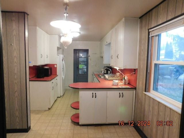 kitchen featuring white refrigerator, white cabinetry, and wooden walls