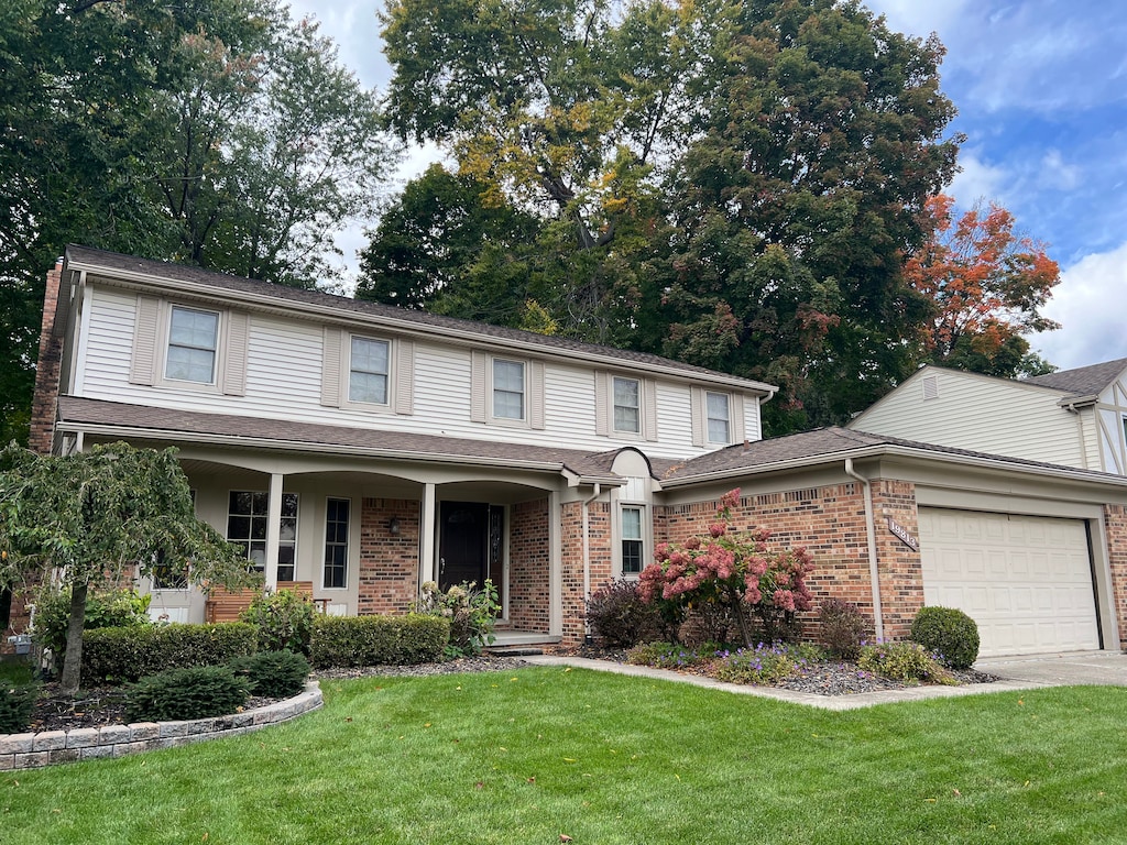 view of property with covered porch, a garage, and a front yard