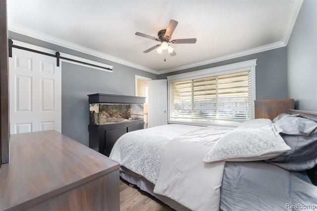 bedroom with light wood-type flooring, a barn door, ceiling fan, and ornamental molding