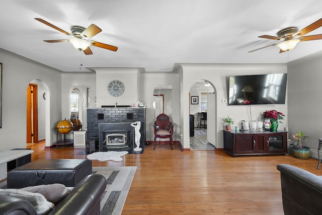 living room with light hardwood / wood-style floors, a wood stove, and ceiling fan