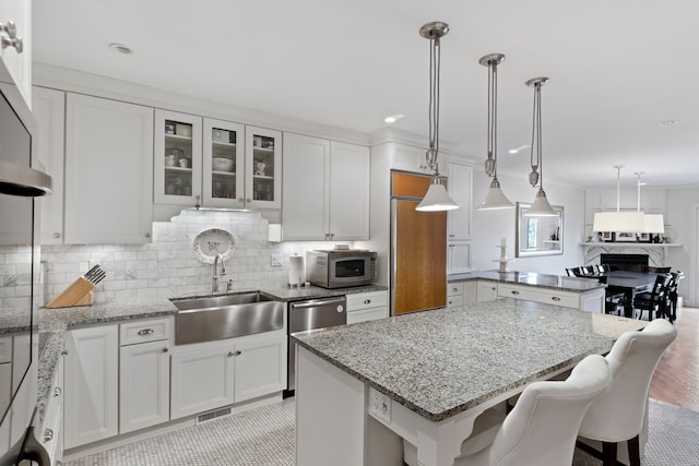 kitchen with white cabinetry, hanging light fixtures, light stone counters, backsplash, and a kitchen bar