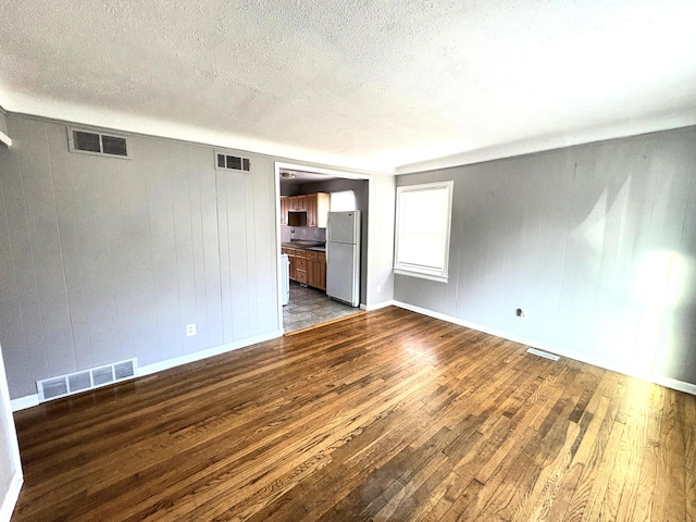 unfurnished living room featuring a textured ceiling, hardwood / wood-style flooring, and wooden walls