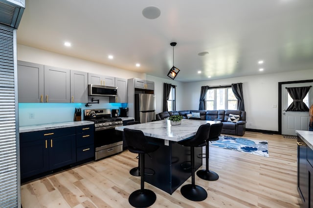 kitchen with light stone countertops, appliances with stainless steel finishes, light hardwood / wood-style flooring, a center island, and a breakfast bar area